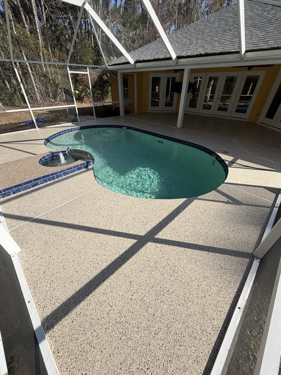 Tan decorative pool deck surrounding a screened swimming pool